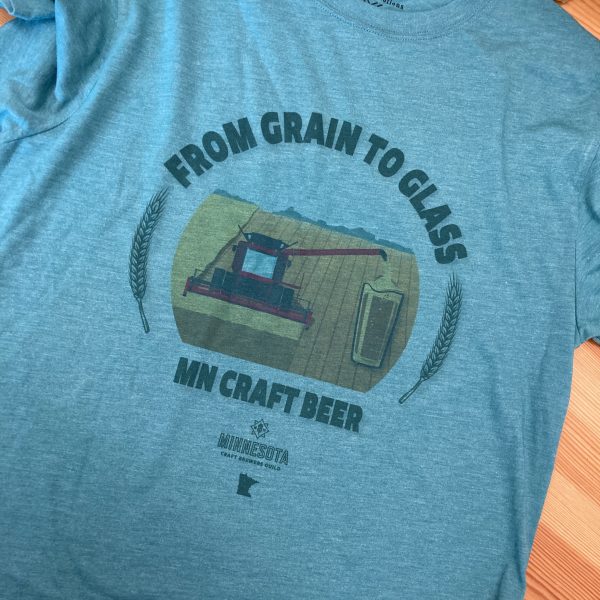 Green shirt with rounded text saying "From Grain to Glass" above an image of a combine harvesting a field; the grain from the unloader is coming out as beer and pouring directly into a pint glass. Below the design are the words "MN Craft Beer" and the MNCBG logo and state outline.